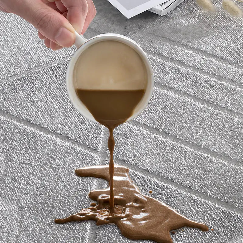 Close-up of waterproof grey geometric-patterned rug repelling spilled coffee, highlighting its stain-resistant and easy-clean features