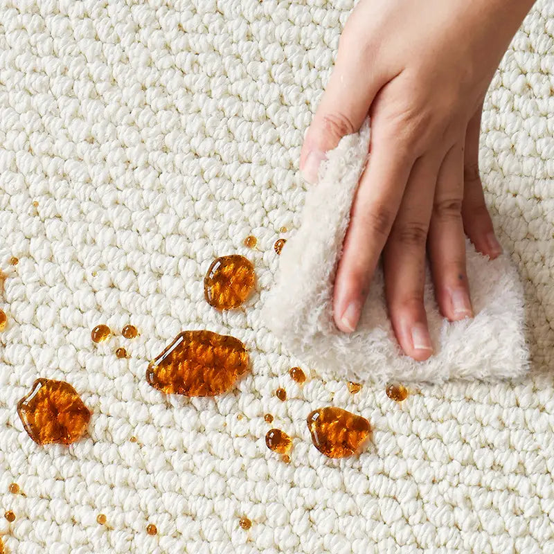 Close-up of a waterproof wool rug being easily cleaned, showing stain-resistant surface