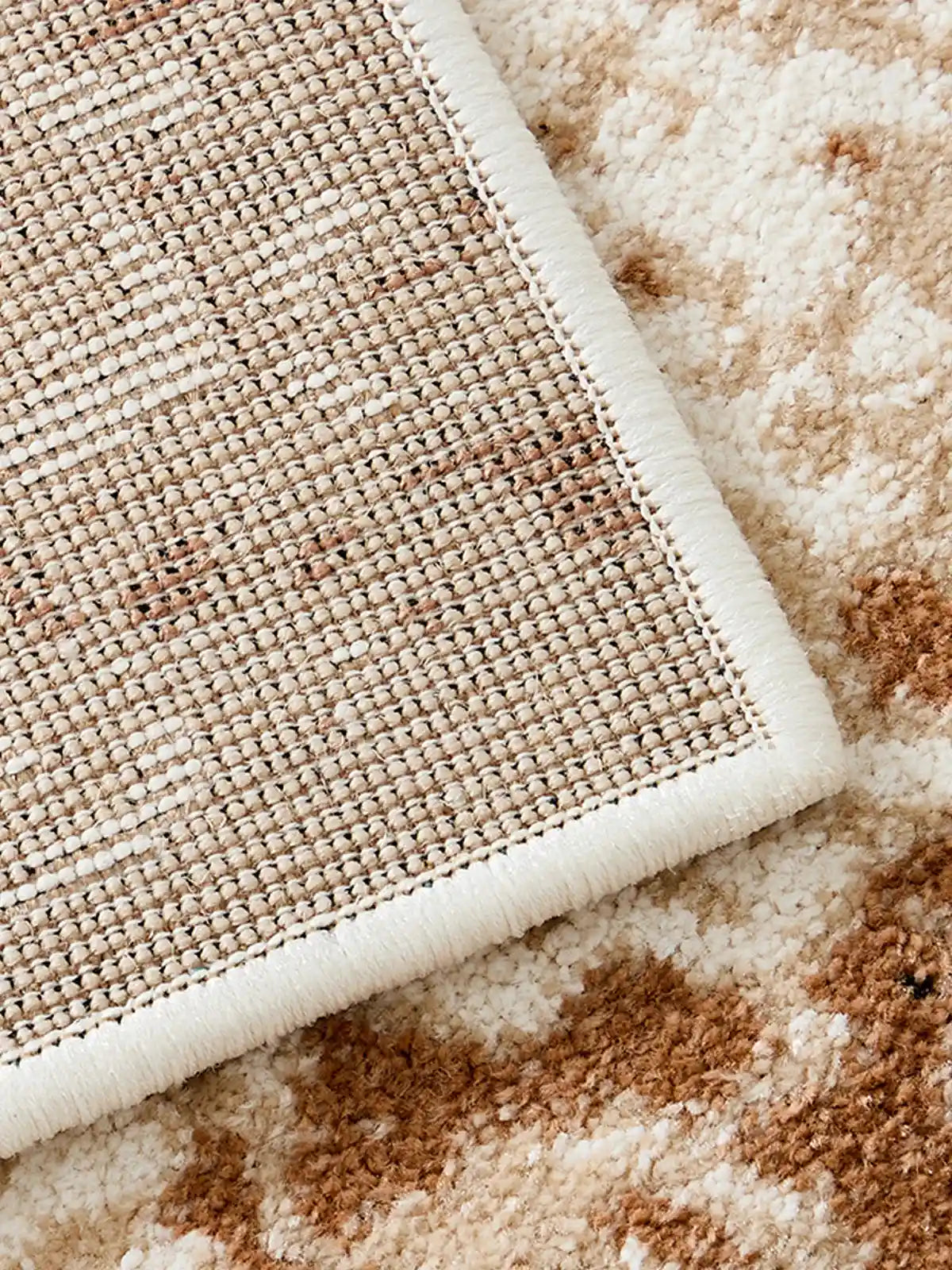 Close-up of woven backing and stitched edge of beige rug showing durable no-glue construction